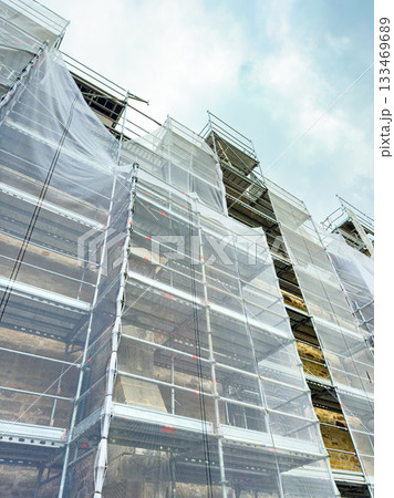 Construction site with scaffolding and protective covering under a cloudy sky in an urban area Construction site with scaffolding and protective covering under a cloudy sky in an urban area 133469689