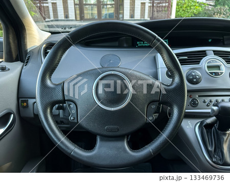 Steering wheel of a modern vehicle showcasing the interior design and controls in an urban setting during a sunny afternoon 133469736