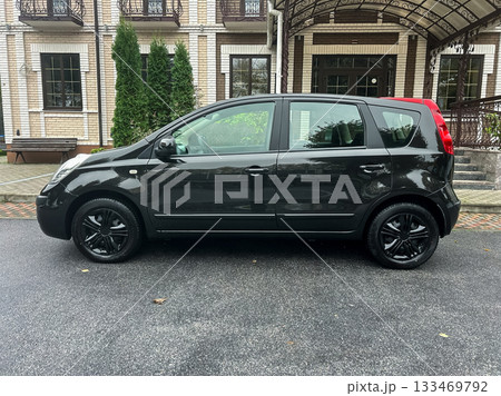 Compact black car parked under a canopy outside a stylish building surrounded by greenery on a rainy day Compact black car parked under a canopy outside a stylish building surrounded by greenery on a rainy day 133469792