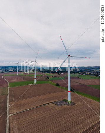 Wind turbines stand gracefully in a vast field under an overcast sky, symbolizing renewable energy efforts while embracing the tranquility of rural landscapes 133469858