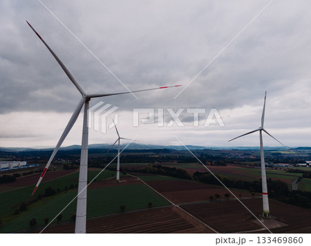 Captivating view of towering wind turbines spinning gracefully above lush fields on an overcast day Captivating view of towering wind turbines spinning gracefully above lush fields on an overcast day 133469860