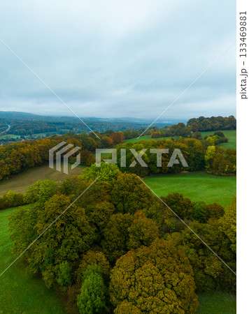 Vibrant autumn landscape unfolds across rolling hills and lush forests beneath a cloudy sky in a rural countryside setting 133469881