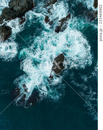 Powerful ocean waves crash against rugged rocks in a breathtaking scene of nature's beauty and strength captured from above 133469902