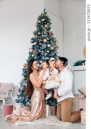 Family celebrates Christmas together by a beautifully decorated tree in a cozy indoor setting with warm lights creating a festive atmosphere 133478823