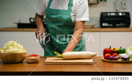 Close-up of hands slicing fresh radish in the kitchen, cooking prep. Close-up of hands slicing fresh radish in the kitchen, cooking prep. 133478993