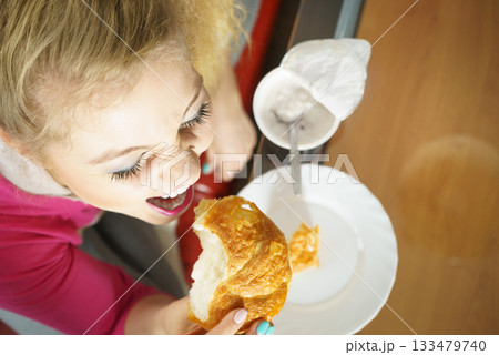 Woman eating croissant and yoghurt Woman eating croissant and yoghurt 133479740