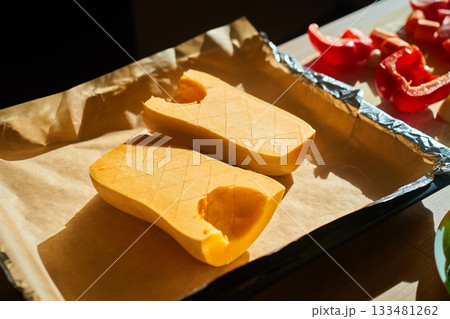 Halved pumpkin on baking tray with parchment paper before roasting 133481262