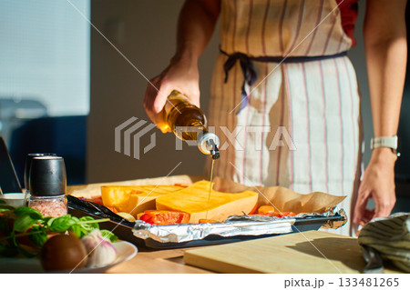 Woman pouring olive oil over pumpkin and vegetables in kitchen 133481265