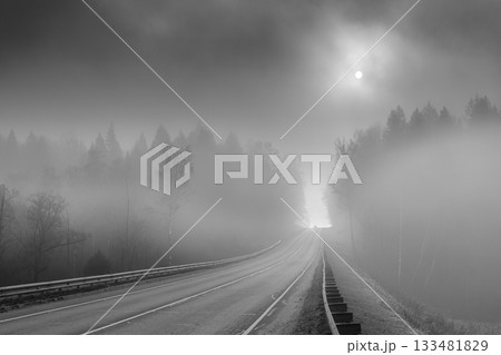 An asphalt road stretching into the distance through a foggy forest. An asphalt road stretching into the distance through a foggy forest. 133481829