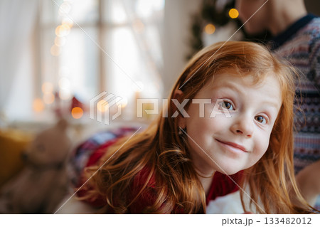 Portrait of small girl indoors at home at Christmas, wearing pyjamas. 133482012