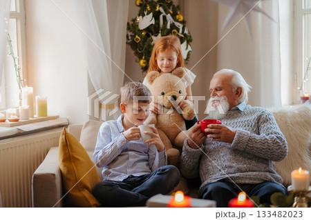 Kids spending Christmas time with senior grandfather indoors at home. Kids spending Christmas time with senior grandfather indoors at home. 133482023