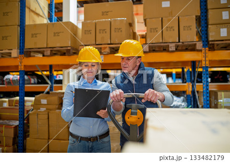Older manager talking with worker in a warehouse, reading plan document. Older manager talking with worker in a warehouse, reading plan document. 133482179