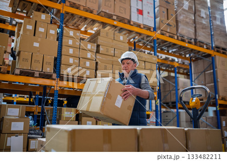Senior male warehouse worker unloading boxes from a pallet truck. Senior male warehouse worker unloading boxes from a pallet truck. 133482211
