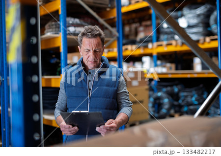 Older warehouse worker working looking at document in clipboard. Older warehouse worker working looking at document in clipboard. 133482217