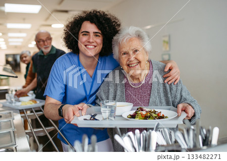 Senior woman having lunch with supportive caregiver in community center cafeteria. Senior woman having lunch with supportive caregiver in community center cafeteria. 133482271