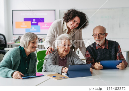 Group of seniors learning digital skills with tutor support in community center. 133482272