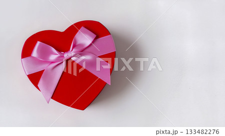 Red heart-shaped gift box tied with a pink satin bow on a white background. 133482276
