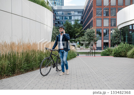 Male cyclist making phone call, walking by his bike. 133482368