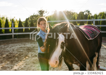 Girl grooming a horse at sunset. 133482421