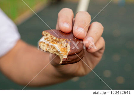 half of small round sponge cake with chocolate in man hand. Two layers of sponge cake with a marshmallow (or souffle) layer, covered in chocolate glaze. 133482641