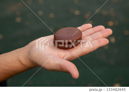 Airy sponge cake with delicate cream inside, covered in chocolate glaze in man hand. small round sponge cake with chocolate. 133482645