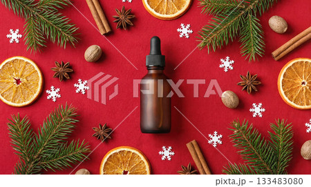 Brown glass dropper bottle surrounded by festive decorations including dried orange slices, pine branches, and spices on a vibrant red background Brown glass dropper bottle surrounded by festive decorations including dried orange slices, pine branches, and spices on a vibrant red background 133483080