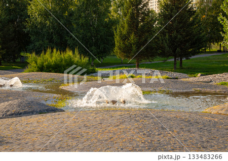 modern water fountain in the garden, lush greenery and stone pathways. The warm light of sunset enhances the calm ambiance of the area. 133483266