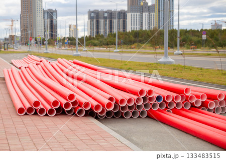 bright red new conduit plastic pipes on the street. Modern buildings rise in the background, urban development bright red new conduit plastic pipes on the street. Modern buildings rise in the background, urban development 133483515