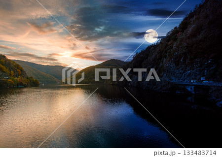 mountainous landscape with lake on autumn equinox. day and night time change concept. forest on hills near the shore of river under sky with moon at twilight. beautiful view of stunning place mountainous landscape with lake on autumn equinox. day and night time change concept. forest on hills near the shore of river under sky with moon at twilight. beautiful view of stunning place 133483714