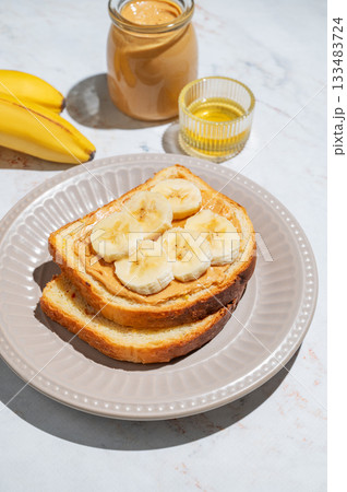Peanut butter sandwich and banana on a plate on a marble background with fruits and honey. 133483724