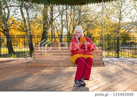 A body positive woman sits on swing and drinks coffee. A 47-year-old Caucasian woman, mother of many children, relaxes alone on a bright autumn day. Mental health, harmony with oneself and the world A body positive woman sits on swing and drinks coffee. A 47-year-old Caucasian woman, mother of many children, relaxes alone on a bright autumn day. Mental health, harmony with oneself and the world 133483898