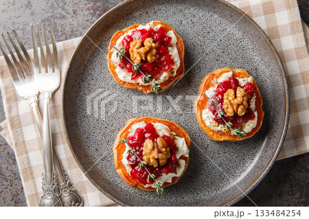 Delicious baked sweet potato with cream cheese, cranberry sauce, thyme and walnuts close-up in a plate. Horizontal top view 133484254