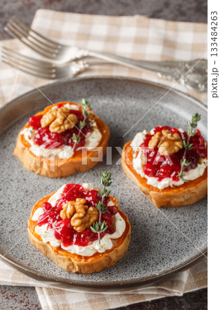 baked sweet potato appetizer with cream cheese, cranberry jam, spices and walnuts close-up in a plate. Vertical 133484263