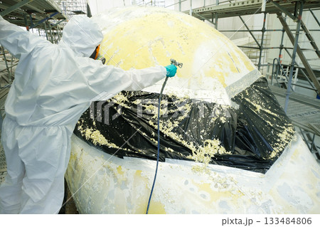 Worker applies protective coating to aircraft surface inside hangar during maintenance procedures at aerospace facility 133484806
