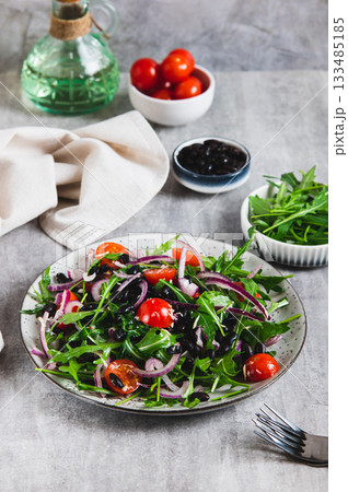 Fresh salad with black beans, cherry tomatoes, arugula and red onion on a plate vertical view 133485185