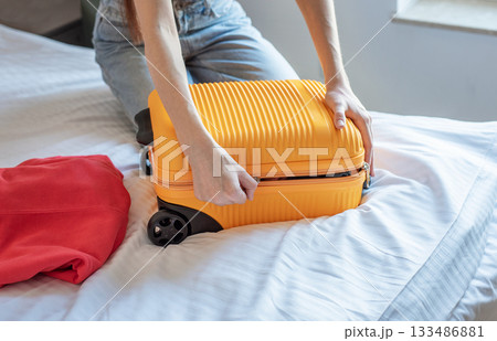 Woman packing suitcase on bed preparing for travel Woman packing suitcase on bed preparing for travel 133486881