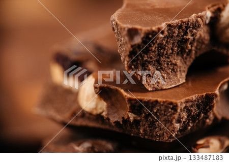 Close-up stacked chocolate pieces with crunchy texture and nuts on warm brown background for dessert branding and confectionery advertising Close-up stacked chocolate pieces with crunchy texture and nuts on warm brown background for dessert branding and confectionery advertising 133487183