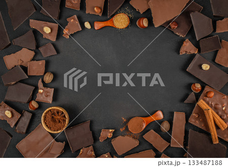 Chocolate pieces, nuts, cocoa powder and spices arranged around empty dark background with ample copy space for dessert menus, branding or advertising 133487188