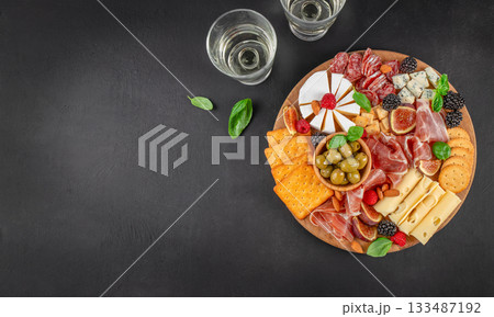 Elegant charcuterie board with assorted cheeses, cured meats, crackers, olives, figs, berries and wine on dark background with copy space 133487192