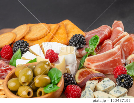 Assorted gourmet cheese charcuterie board with prosciutto, brie, blue cheese, olives, figs, crackers and fresh berries for appetizer or wine tasting 133487195