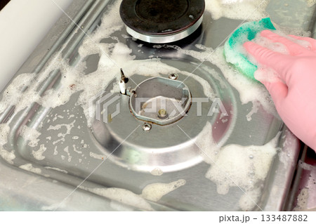 Cleaning a stainless steel gas stove with a sponge and soapy water. Hygiene and home care. Cleaning a stainless steel gas stove with a sponge and soapy water. Hygiene and home care. 133487882