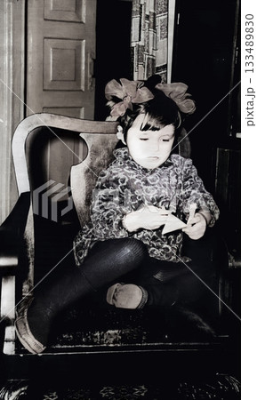 Vintage portrait of little girl with bows and velvet dress sitting in a chair. Retro photo from 1972. Vintage portrait of little girl with bows and velvet dress sitting in a chair. Retro photo from 1972. 133489830