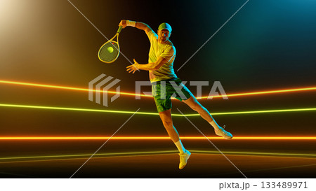 Jumping tennis player performing backhand in mid-air illuminated by colored lights. Handmade collage Jumping tennis player performing backhand in mid-air illuminated by colored lights. Handmade collage 133489971