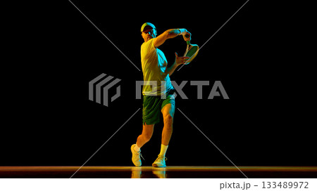 Male tennis player striking forehand with focus and precision in studio light 133489972
