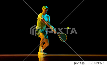 Focused tennis player returning ball with calm concentration under dramatic light 133489973