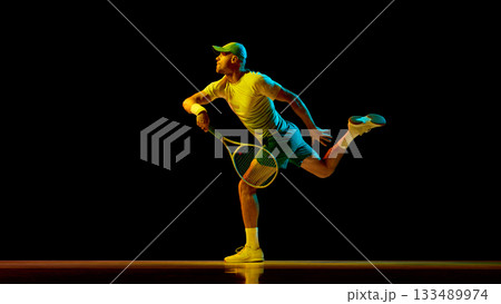 Tennis player stretching to hit low ball under neon light with focus Tennis player stretching to hit low ball under neon light with focus 133489974