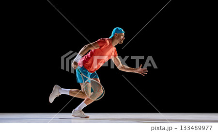 Male tennis player running low preparing for quick backhand shot 133489977