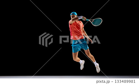 Athletic man jumping for strong tennis shot in professional studio lighting Athletic man jumping for strong tennis shot in professional studio lighting 133489981