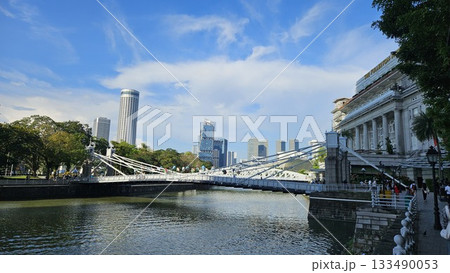A bright riverside scene captures a historic bridge, lush trees, and elegant city architecture under a vivid blue sky with modern skyscrapers rising in the background A bright riverside scene captures a historic bridge, lush trees, and elegant city architecture under a vivid blue sky with modern skyscrapers rising in the background 133490053