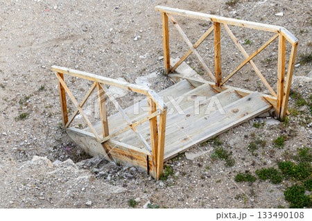 An empty weathered wooden platform with railings and steps sits on a dry ground 133490108